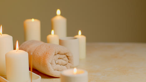 Still-Life-Of-Lit-Candles-With-Green-Plant-Incense-Stick-And-Soft-Towels-As-Part-Of-Relaxing-Spa-Day-Decor